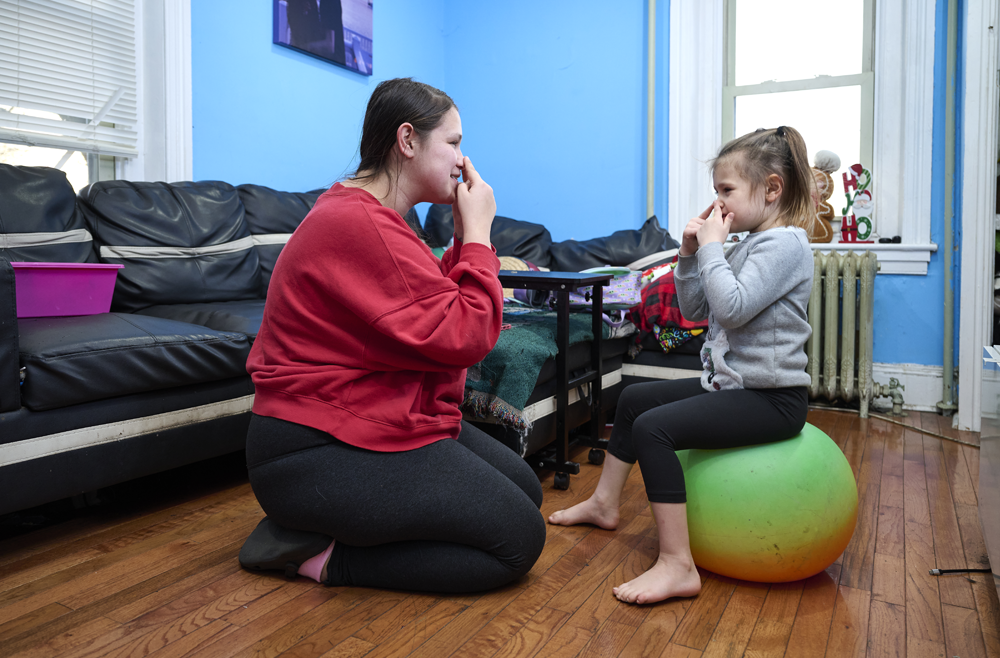 Scarlett Adams and her mom Taylor sit on the floor of their living room, playing with a ball.